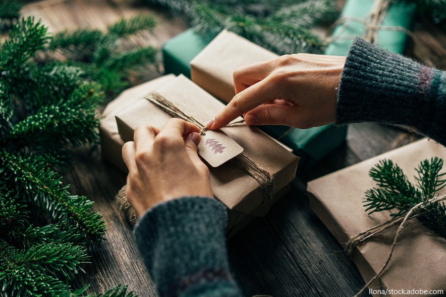 Nahaufnahme von Händen einer Person, die ein Weihnachtsgeschenk mit kleinen Extras verziert.