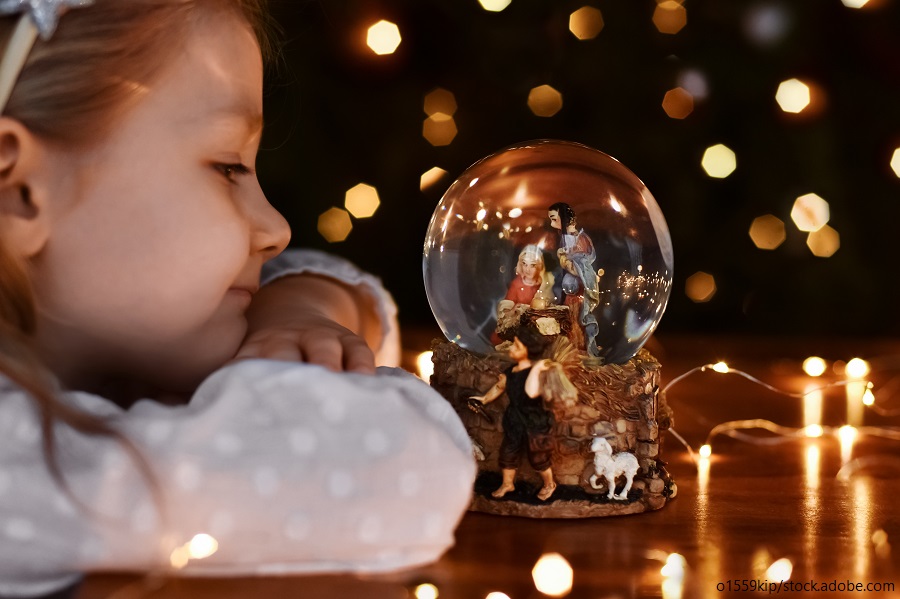 Mädchen blickt auf eine Glaskugel mit Weihnachtskrippe