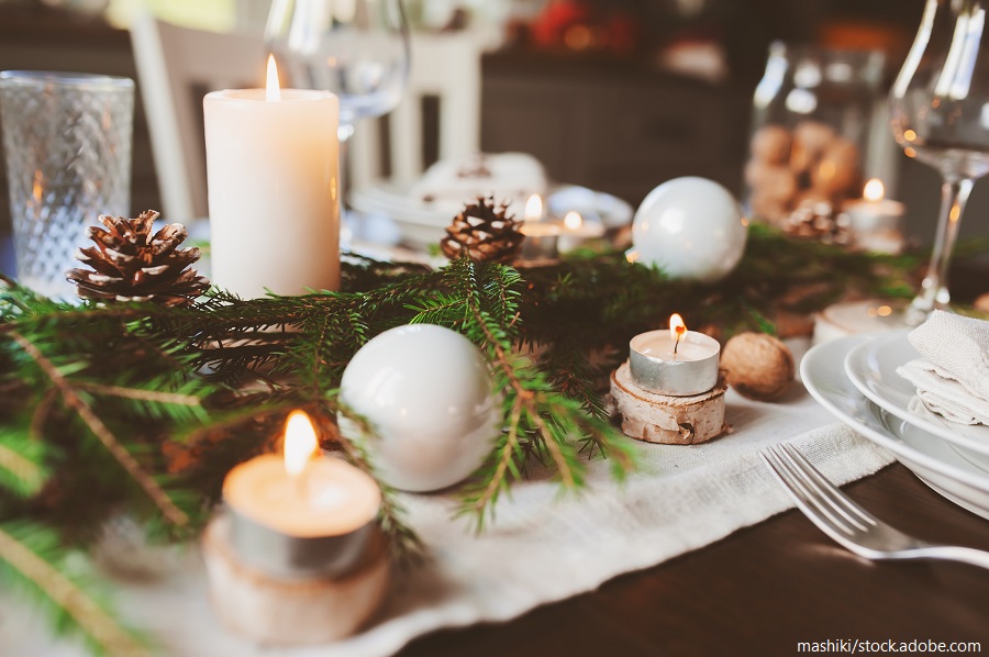Weihnachtliche Tischdekoration mit Kerzen, Tannenzweigen, Tannenzapfen und weißen Kugeln auf einem festlich gedeckten Tisch