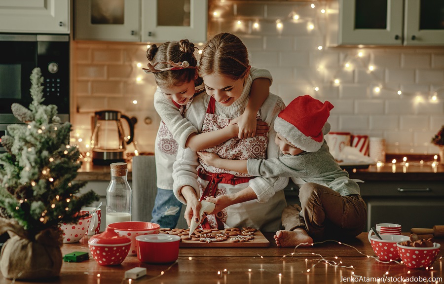 Eine Familie backt gemeinsam Weihnachtsplätzchen in der Küche, umgeben von festlicher Dekoration und Lichtern